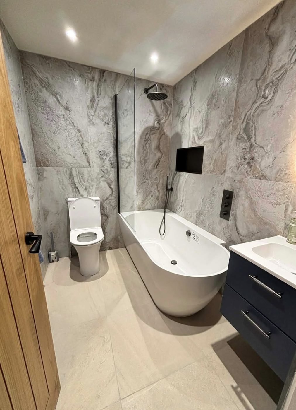 Marble tiled bathroom with a P shaped shower bath, black brassware and navy vanity unit